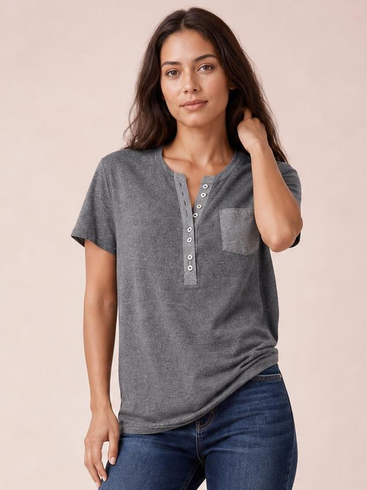 A model wears a gray half-button short-sleeve T-shirt with a relaxed silhouette, button placket, and chest pocket while touching her hair.