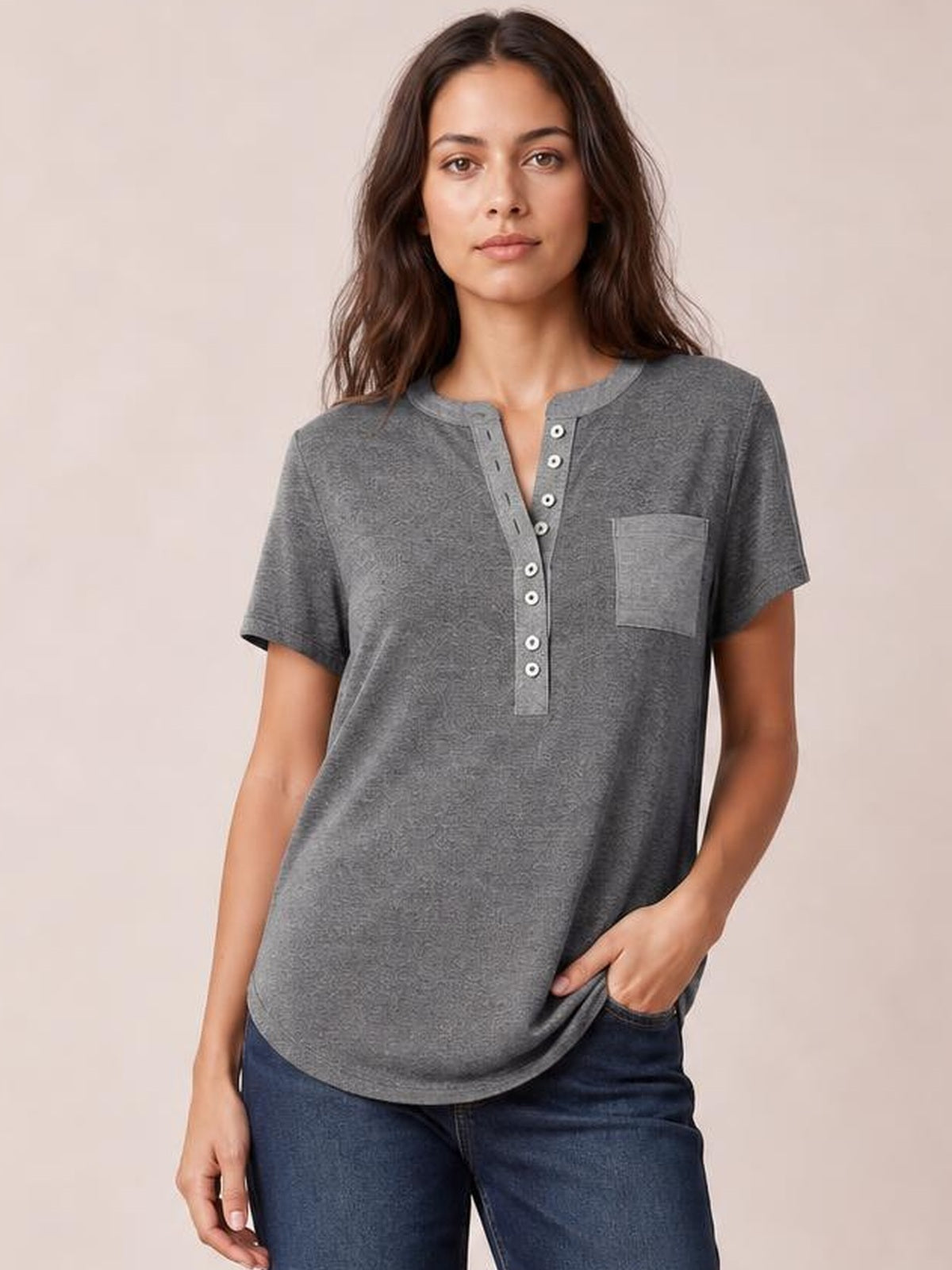 Model wearing a gray half-button short-sleeve T-shirt with a chest pocket, round neckline, relaxed silhouette, and curved hem, posing with one hand in her pocket.