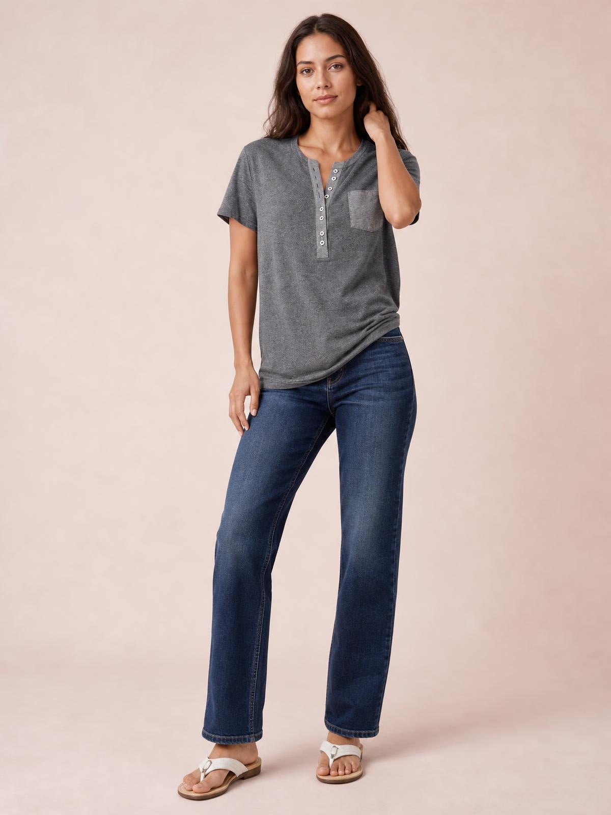 Model wearing a charcoal gray half button short sleeve T-shirt with a chest pocket and relaxed straight silhouette, posing with one hand touching her hair.