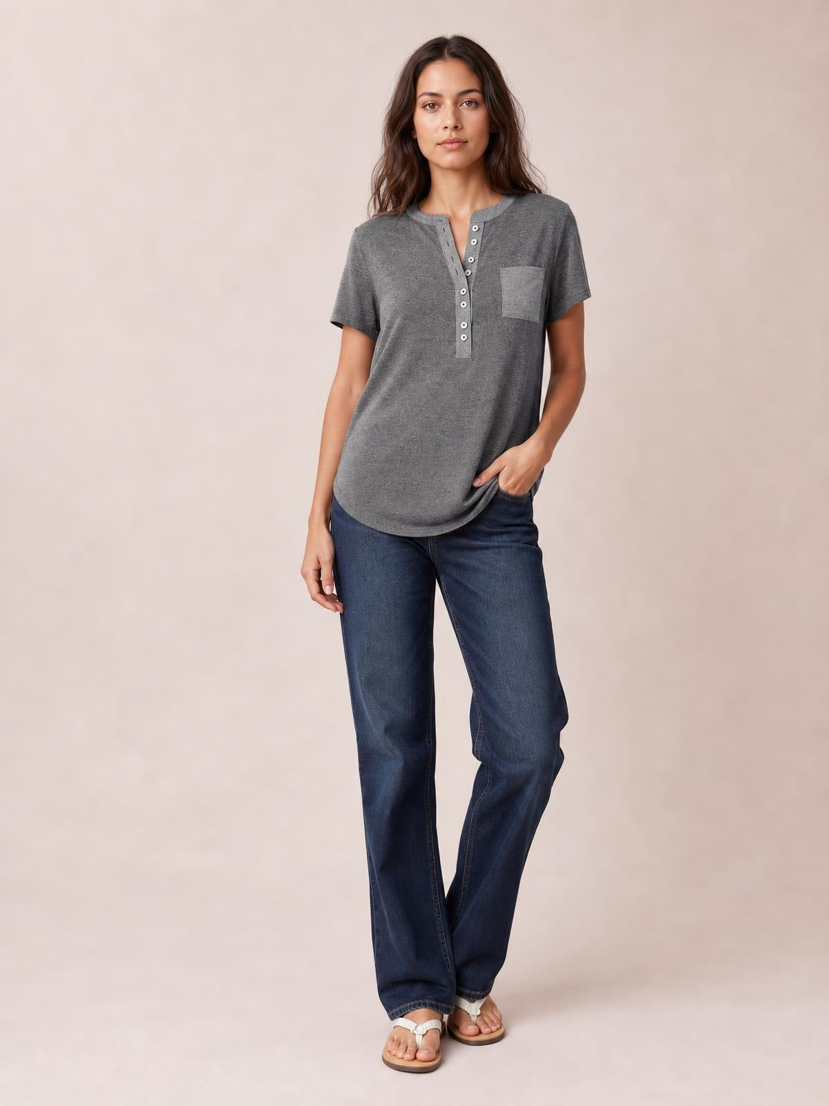 A woman models a gray half-button short-sleeve T-shirt with a chest pocket, relaxed silhouette, curved hem, and one hand resting at the hip.