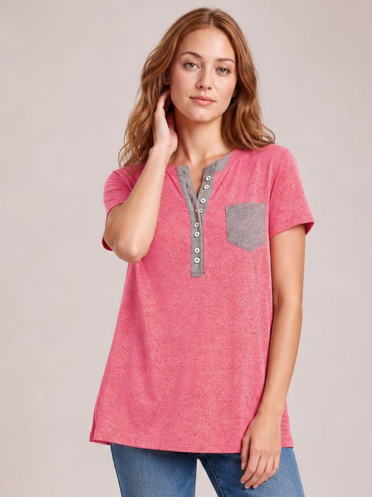 Model poses in a pink short-sleeve T-shirt with a relaxed long silhouette, gray half-button placket, and matching chest pocket.