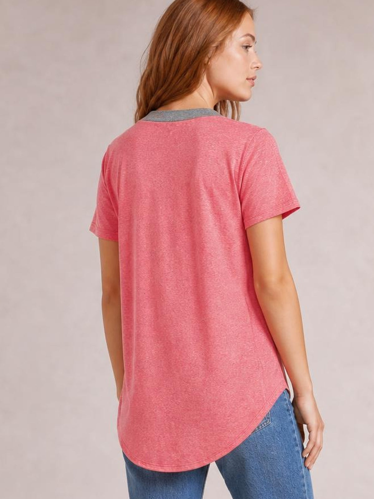 A model turns to show the back of a pink half-button short-sleeve T-shirt with a contrasting gray collar and relaxed silhouette with a curved hem.