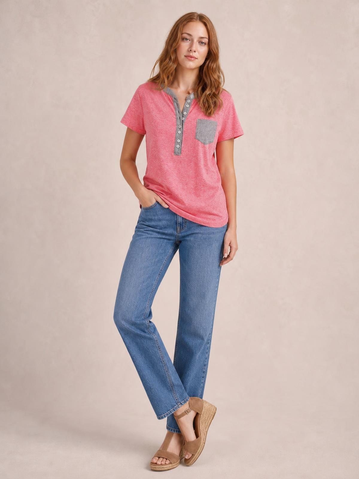 A model poses in a pink half button short sleeve T-shirt with a gray button placket and chest pocket, featuring a relaxed, slightly stretchy silhouette.