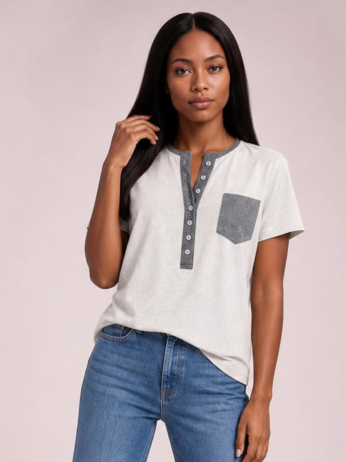 Model wearing an off-white half-button short sleeve T-shirt with a gray contrast placket and chest pocket in a relaxed silhouette, posing with one hand in her hair.