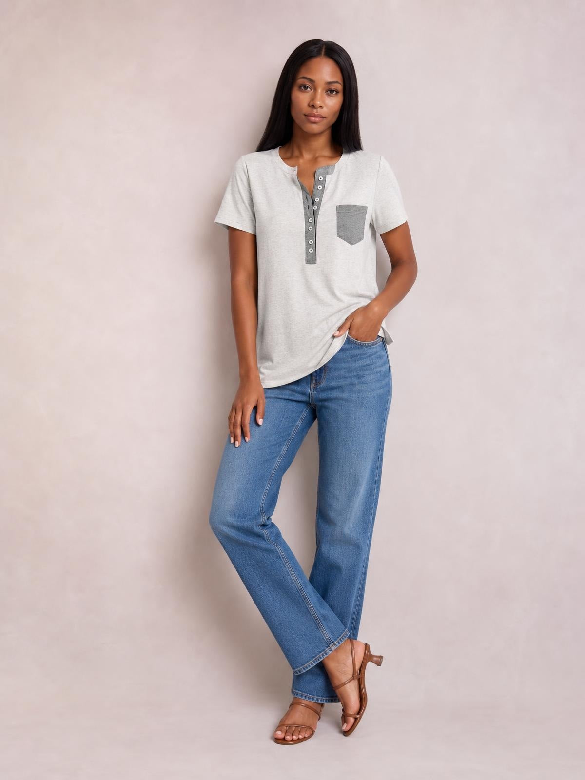 Model wears a light gray half-button short-sleeve T-shirt with a contrasting placket and chest pocket, posed with crossed legs and one hand at the hem.