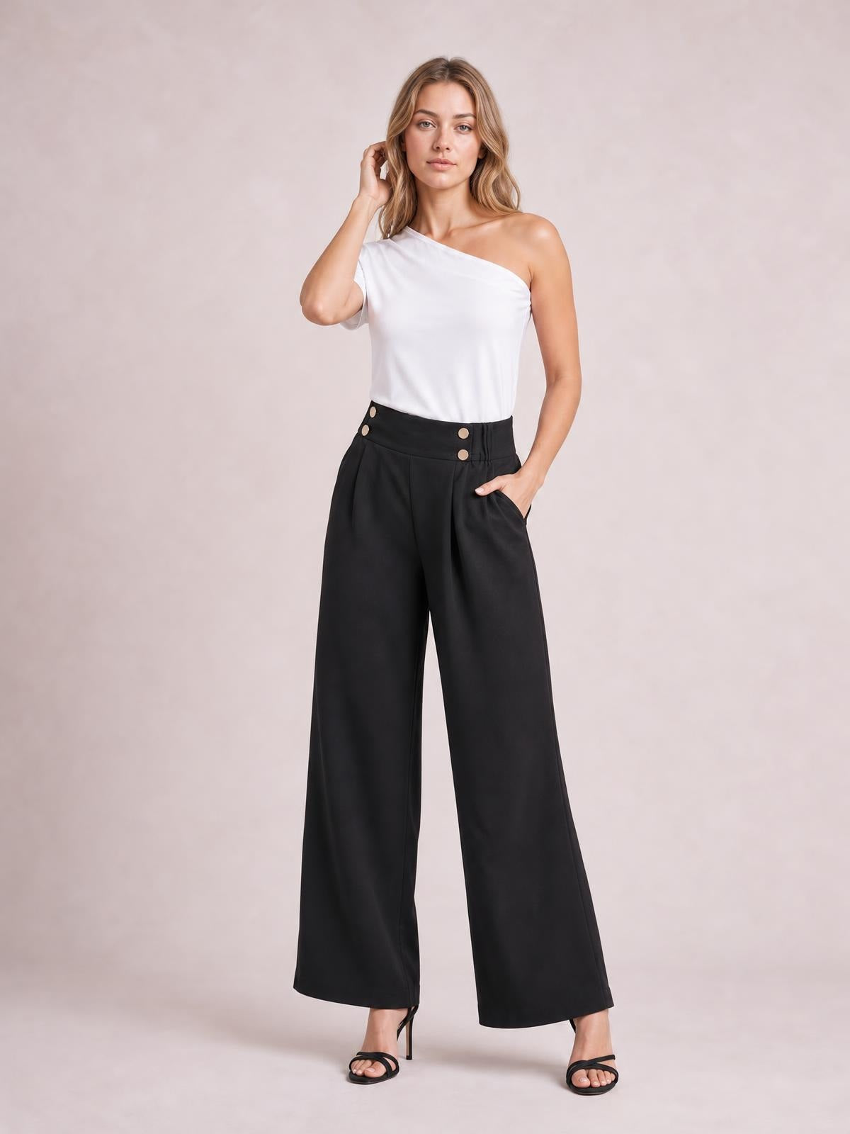 Model poses in black high-waisted wide-leg pants with front button details, pleats, and side pockets, one hand tucked into a pocket.
