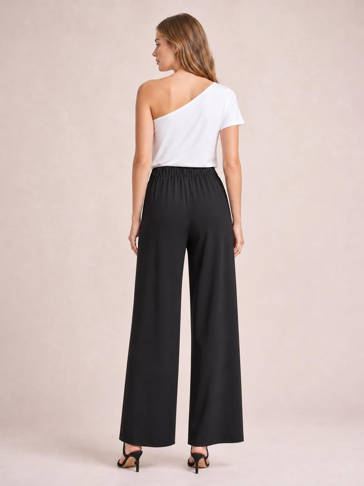 Model viewed from behind wearing black high-waisted wide-leg pants with an elasticized waistband, flowing full-length silhouette, and side pockets.