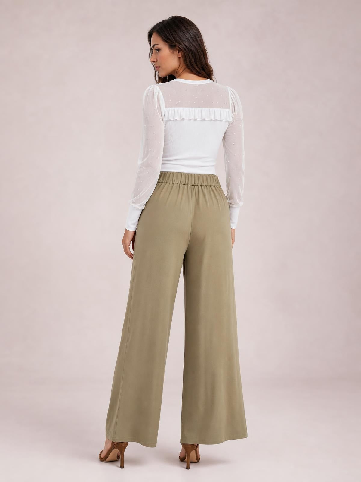 A model is shown from behind in taupe high-waisted wide-leg pants with a gathered elastic waistband and flowing full-length silhouette.