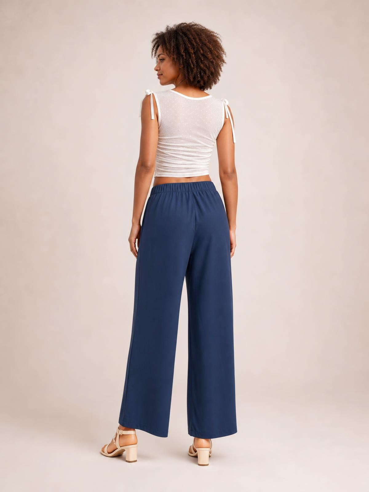 Model shown from the back wears navy high-waisted wide-leg pants with a relaxed full-length silhouette and visible side pockets.