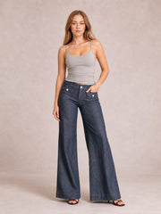 Model poses in dark wash high-waisted wide-leg jeans with buttoned pocket details and a full-length relaxed silhouette.