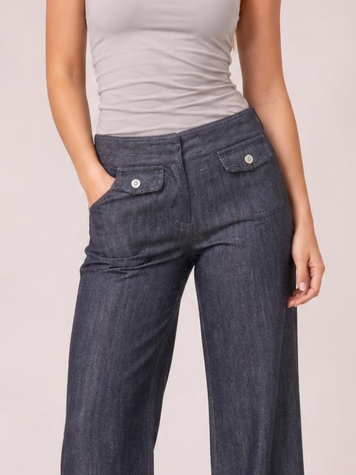 A model wears dark-wash high-waisted wide-leg jeans with a button closure, flap pockets, and a relaxed silhouette, posing with one hand in a pocket.