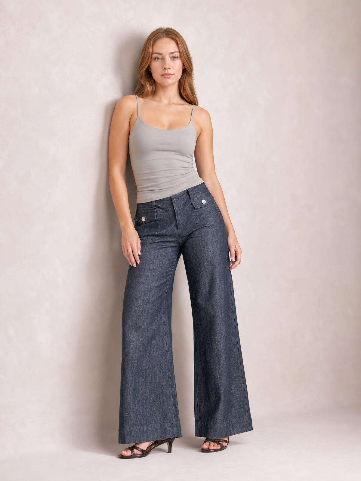 Model leans slightly while wearing dark-wash high-waisted jeans with a buttoned front, pockets, and a relaxed wide-leg silhouette.