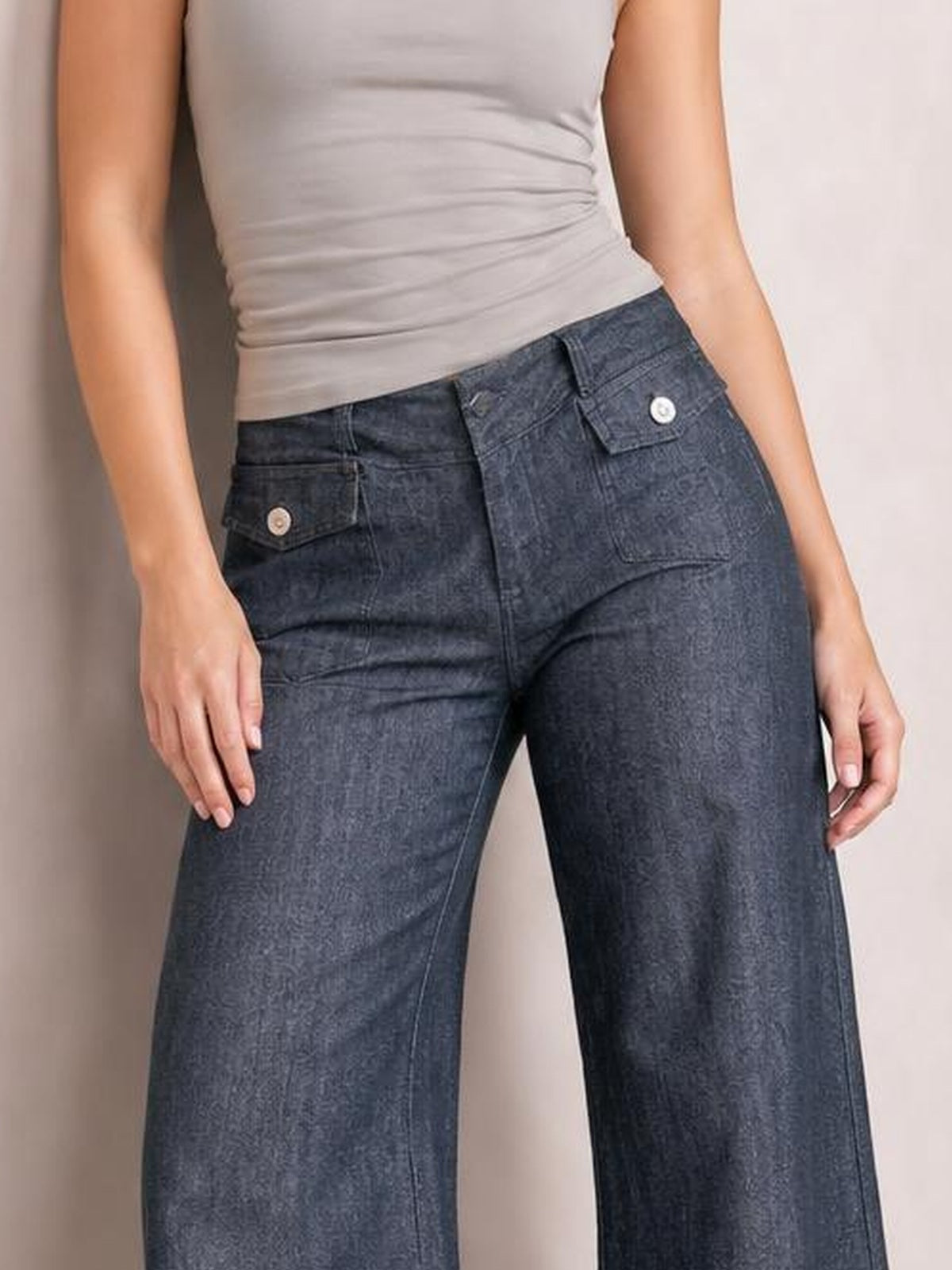 A model wears dark-wash high-waisted wide-leg jeans with a button closure, front flap pockets, and a structured relaxed silhouette, standing with hands at her sides.