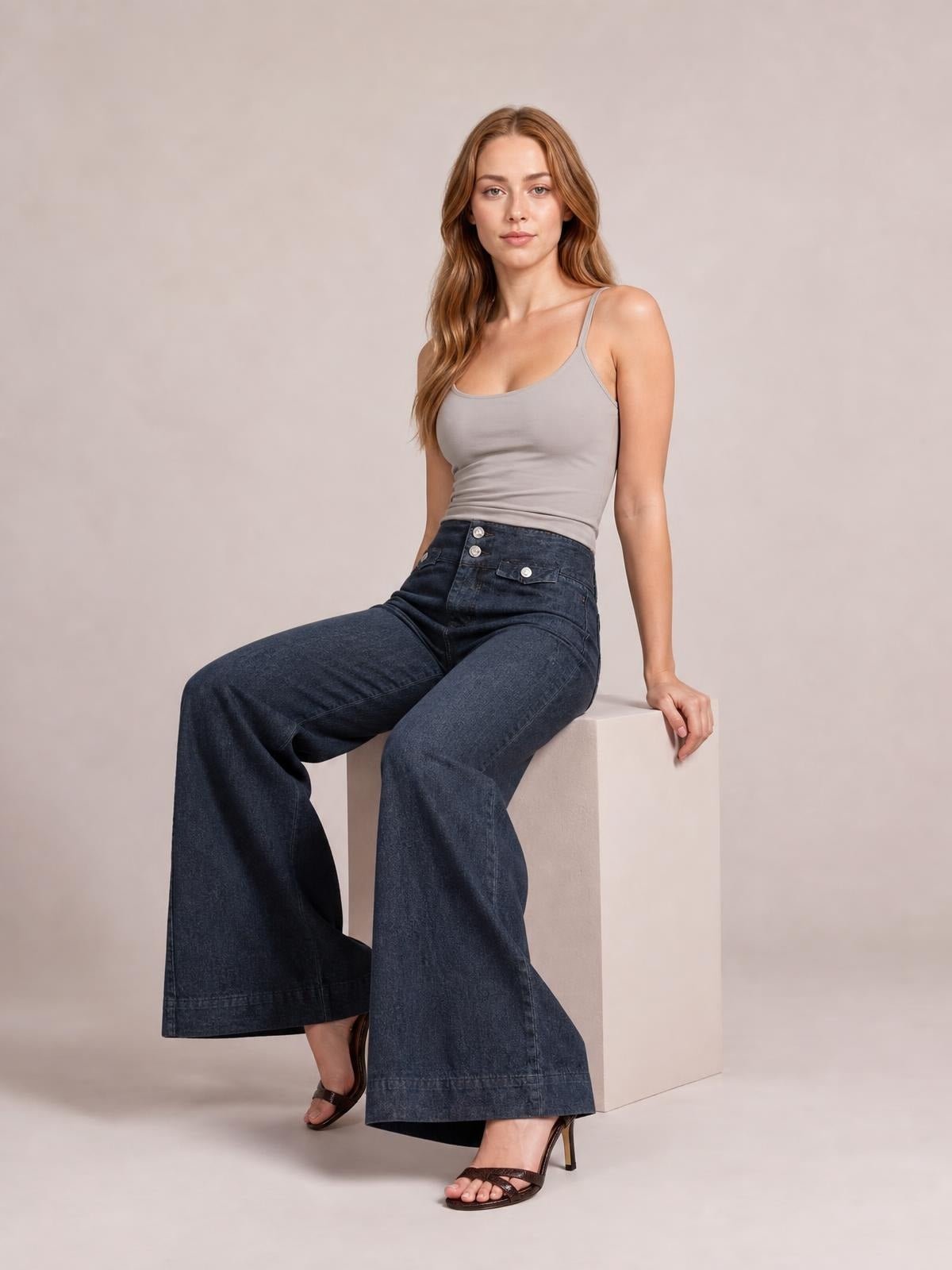 Model seated in dark-wash high-waisted wide-leg jeans with button closure, front pockets, and a structured full-length silhouette.