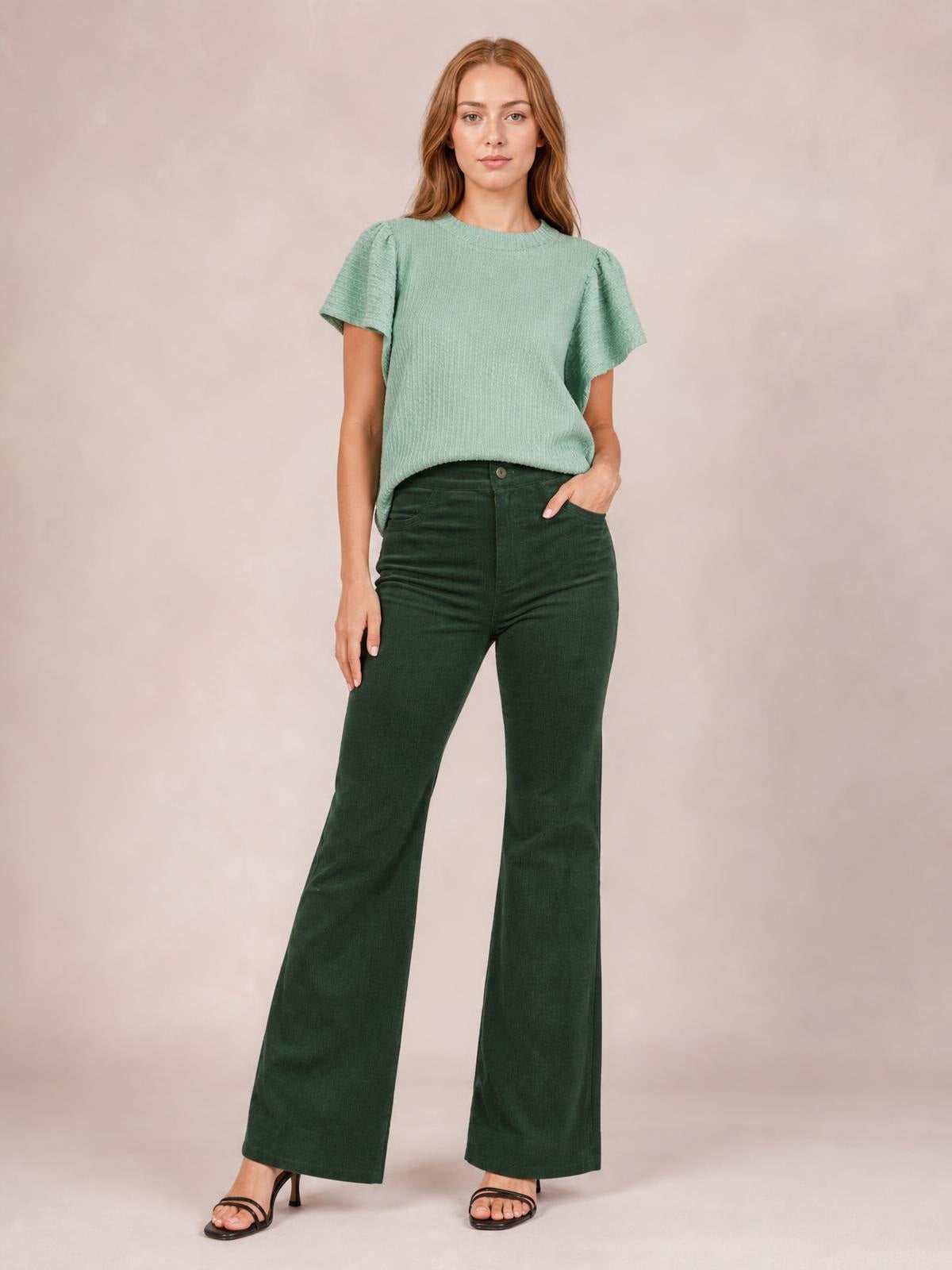 Model poses in dark green high-waist bootcut pants with a fitted hip, button closure, front pockets, and gently flared legs.