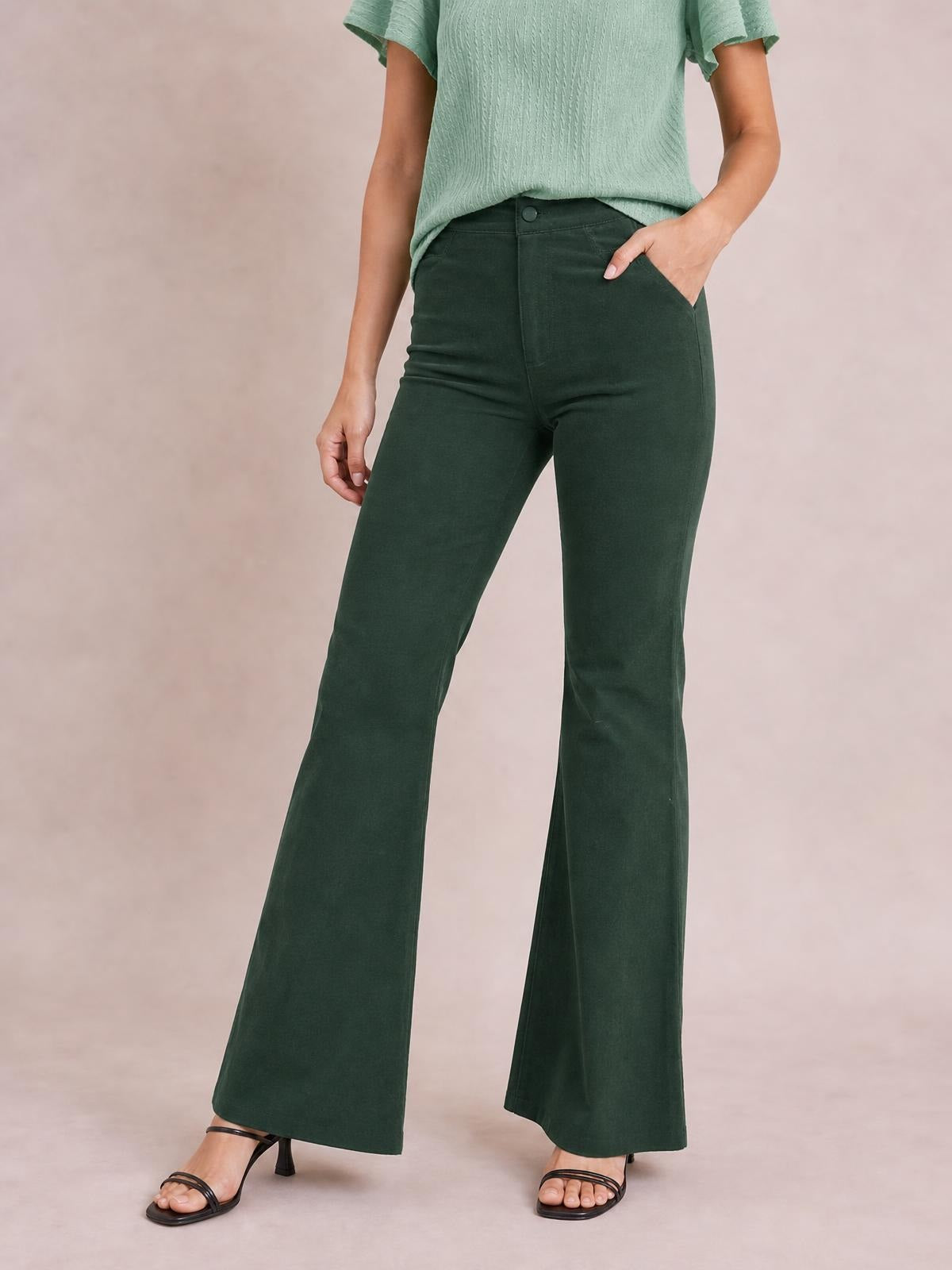 Model poses in dark green high-waist bootcut pants with a button closure, fitted hips and thighs, and gently flared legs.