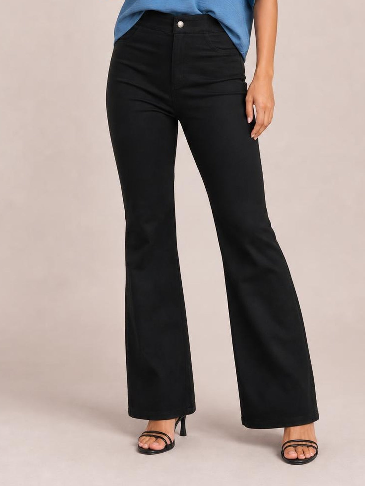 Model wearing black high-waist bootcut pants with a buttoned waistband, front pockets, fitted hips and gently flared legs, standing with one hand at her side.