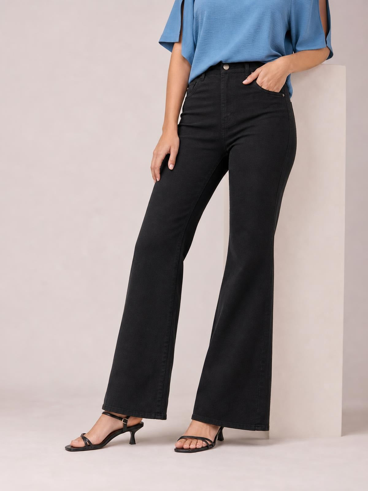A model stands in black high-waist bootcut pants with a fitted hip, front pockets, button closure, and gently flared full-length legs.