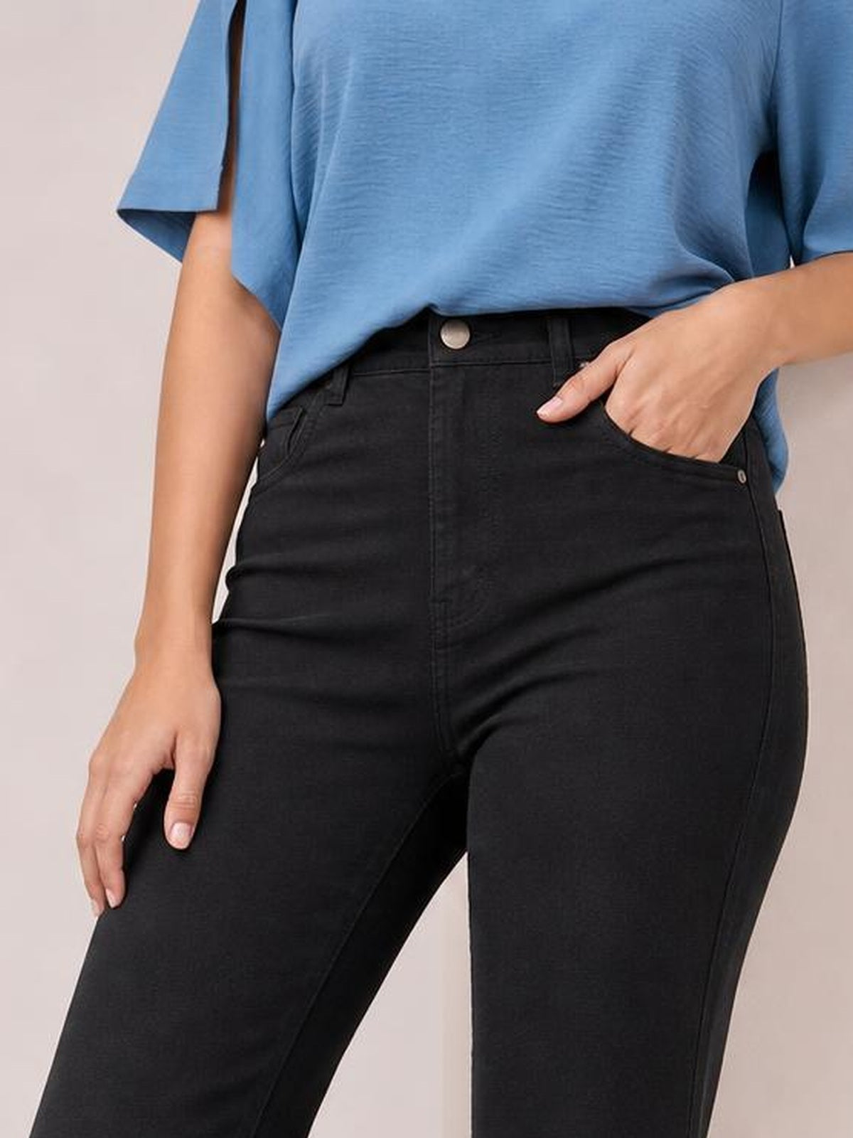 Model wears black high-waist bootcut pants with a fitted hip, belt loops, button closure, front pockets, and one hand tucked into a pocket.