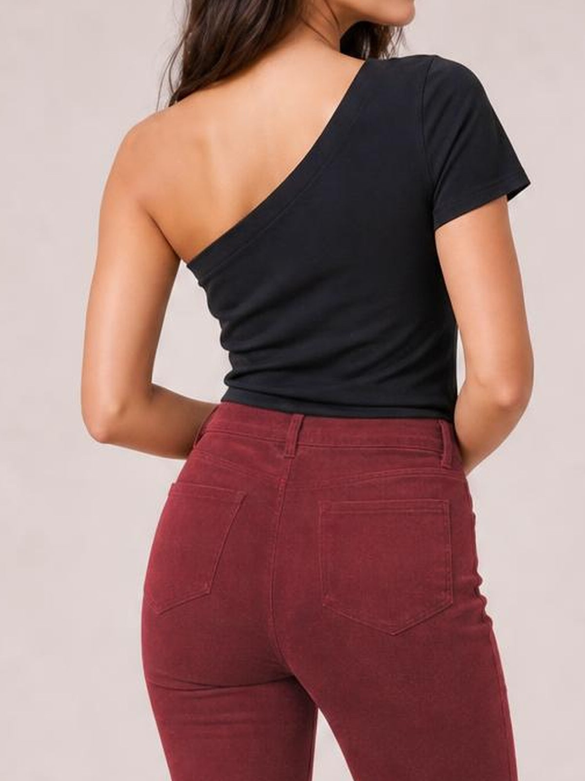 A model poses from the back in burgundy high waist bootcut pants with belt loops, stitched seams, and two rear patch pockets, paired with a black top.
