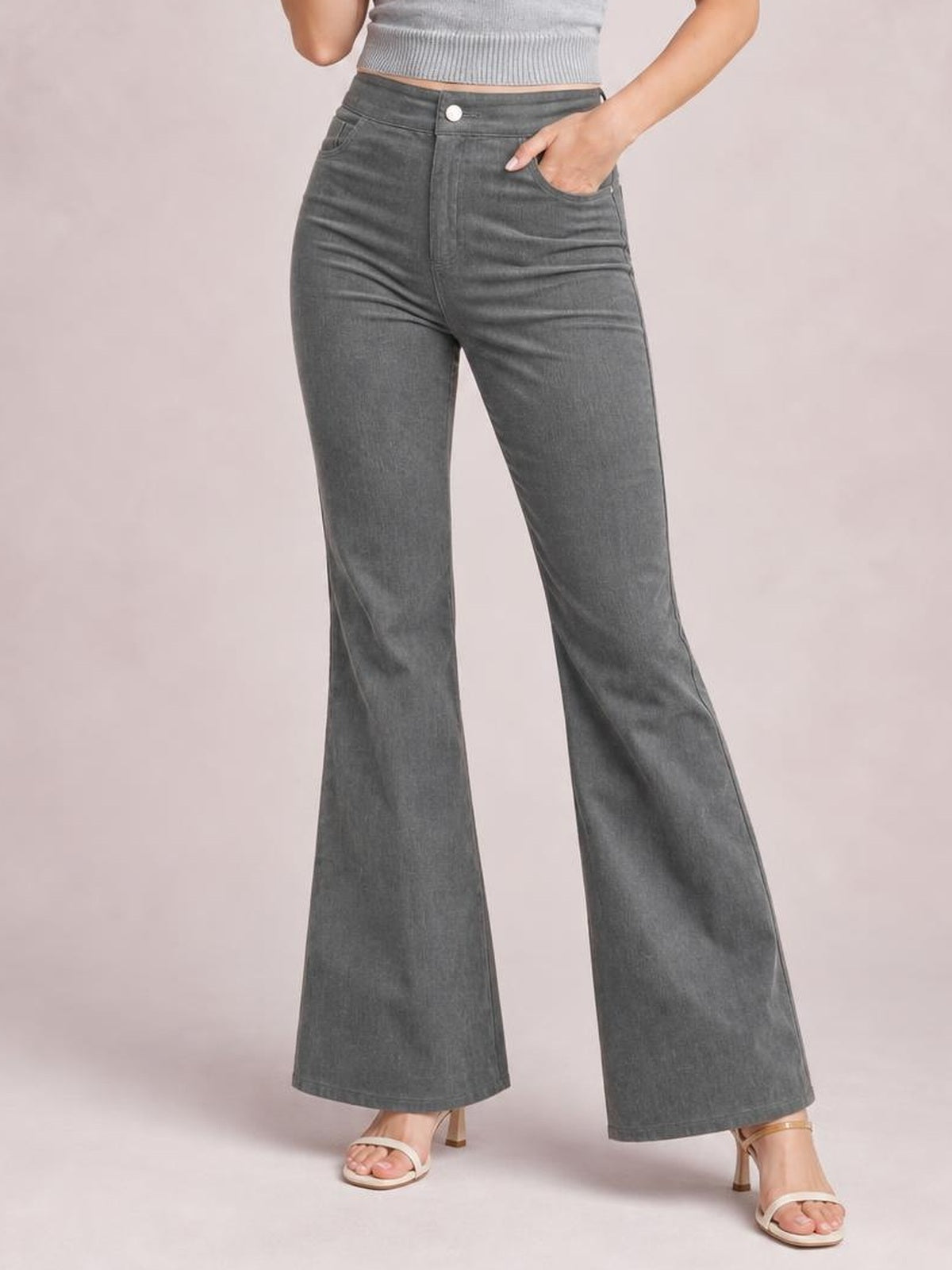 Model poses with one hand in the pocket of gray high-waisted bootcut pants, featuring a button closure, fitted hips, and flared legs.