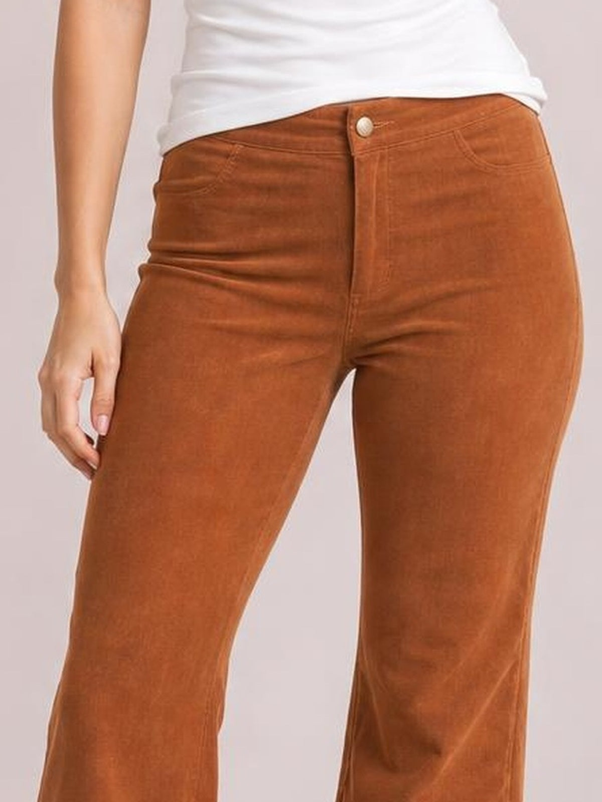 A cropped model wears rust-brown high-waist bootcut pants with a fitted silhouette, front button closure, belt loops, curved pockets, and visible seam detailing.
