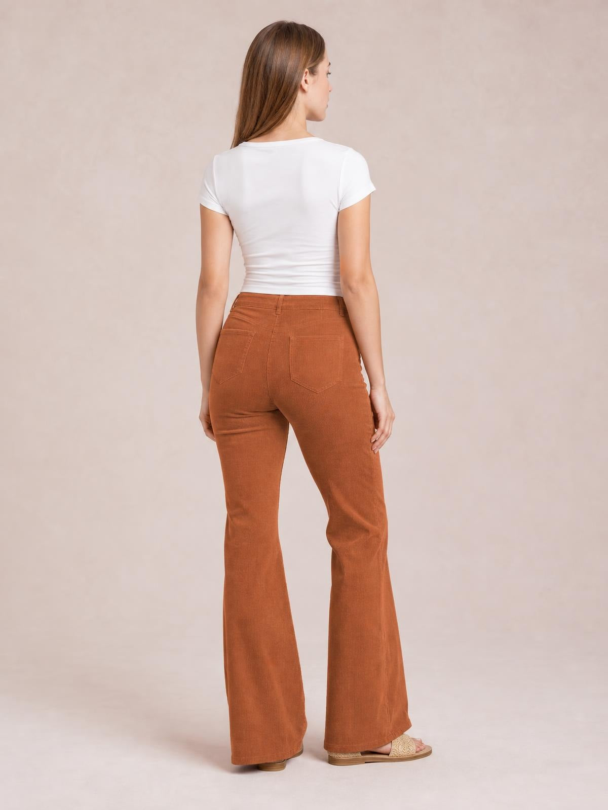 A model poses in a rear view wearing rust-brown high-waist bootcut pants with a fitted silhouette, belt loops, back pockets, and flared hems.