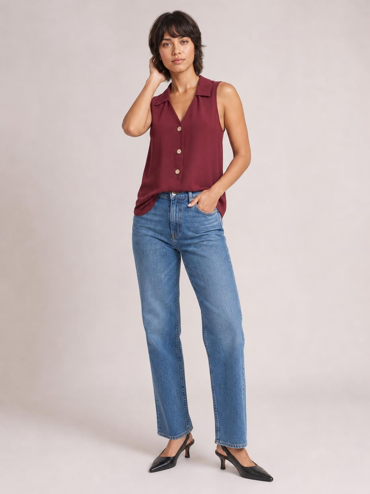 Model poses in a burgundy Johnny collar button-up tank with a sleeveless cut, pointed collar, front buttons, and relaxed straight silhouette over jeans.