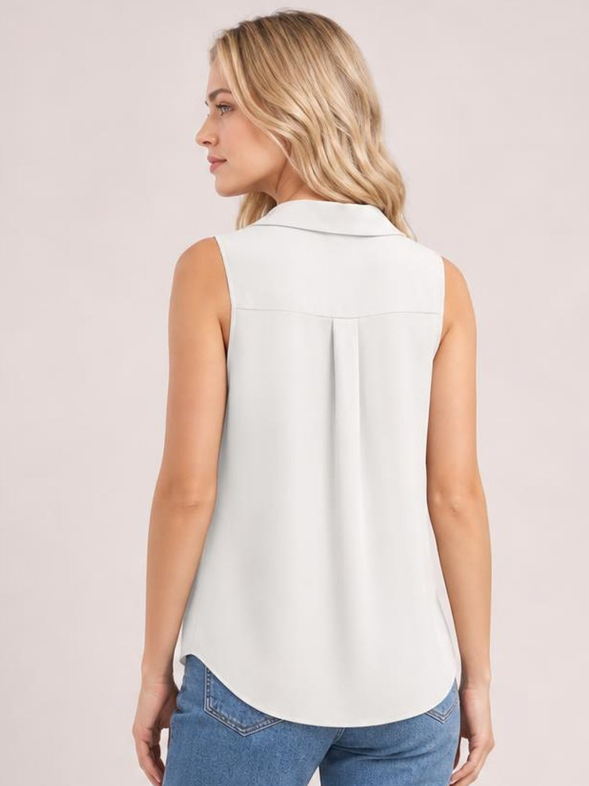 Model poses with her back turned in a white Johnny collar button-up tank featuring a sleeveless cut, back yoke, center pleat, and curved hem.