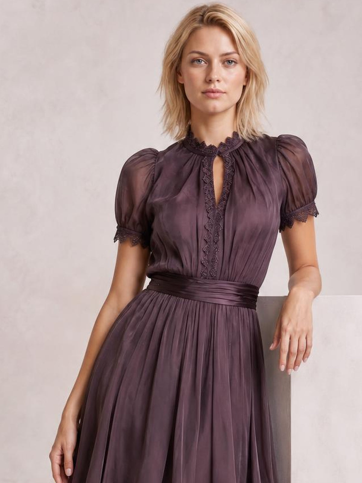 Model poses in a plum A-line dress with puff sleeves, lace-trimmed neckline and cuffs, a keyhole front, defined waist, and pleated full skirt.