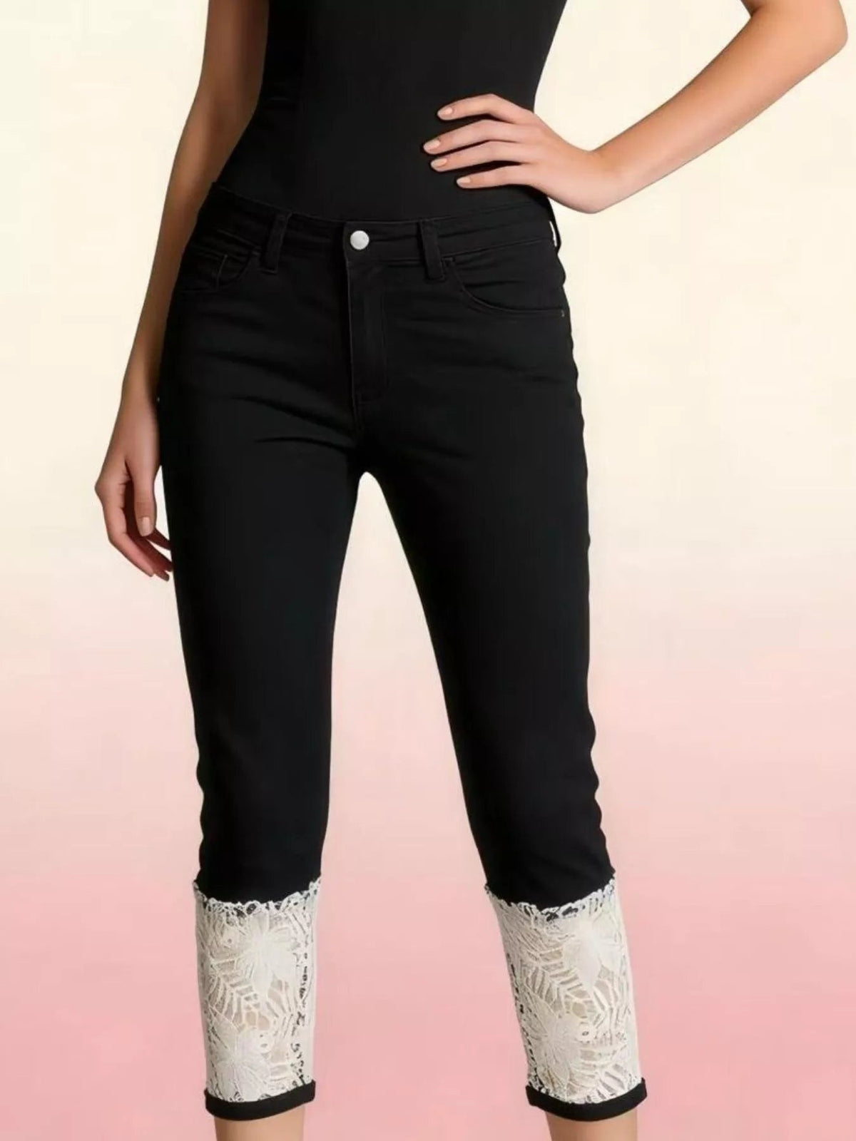 A model poses with one hand on her hip in black lace-trimmed capri jeans featuring a button fly, belt loops, pockets, and a slim silhouette.