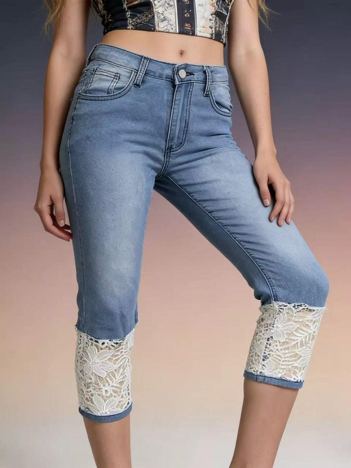 A model wears light blue fitted capri jeans with a button fly, front pockets, and wide white lace-trimmed panels at the cropped hems.