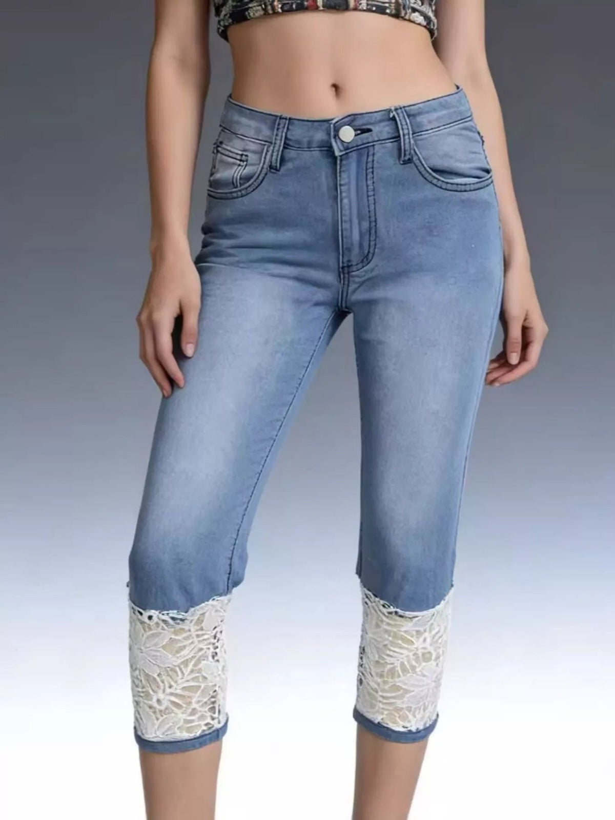 Model stands with hands at her sides wearing light blue lace-trimmed capri jeans with a fitted silhouette, button closure, belt loops, and front pockets.