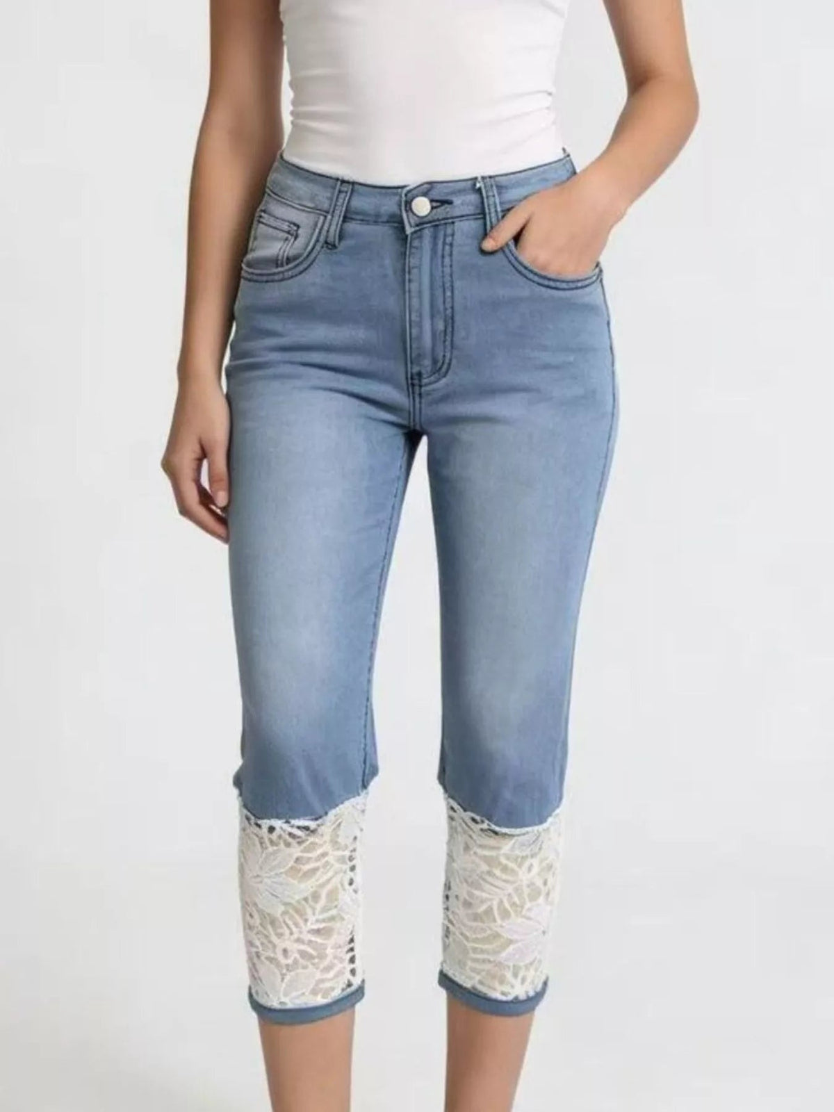 A model wears light blue lace-trimmed capri jeans with a slim silhouette, button closure, front pockets, and intricate lace panels at the cuffs.