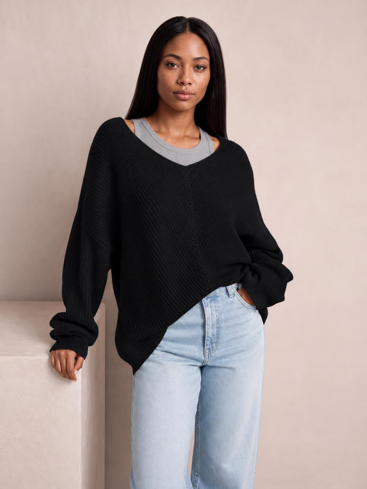 Model wears a black lace-up V-neck sweater with long sleeves, a relaxed oversized silhouette, textured knit construction, and a hand tucked into her jeans pocket.