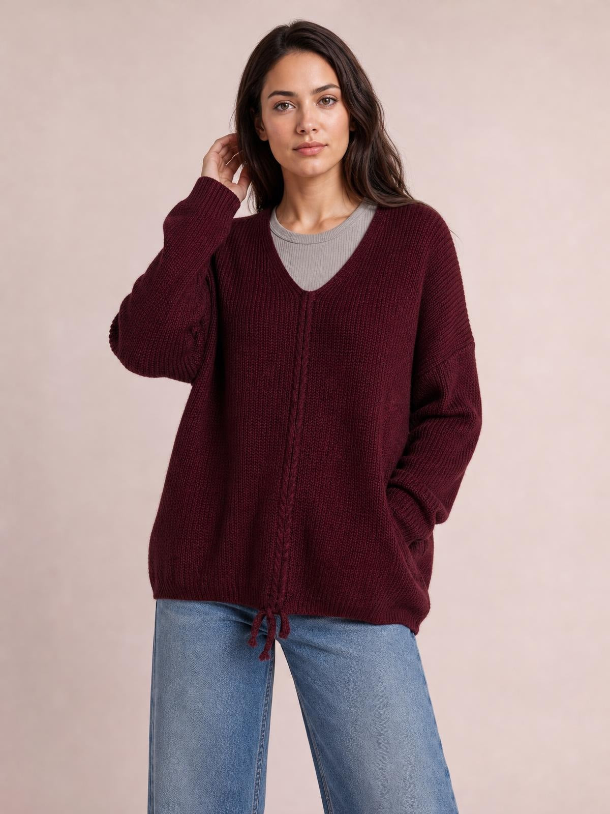 Model poses in a burgundy lace-up V-neck long-sleeve sweater with a relaxed oversized silhouette, textured knit, and tie detail at the hem.