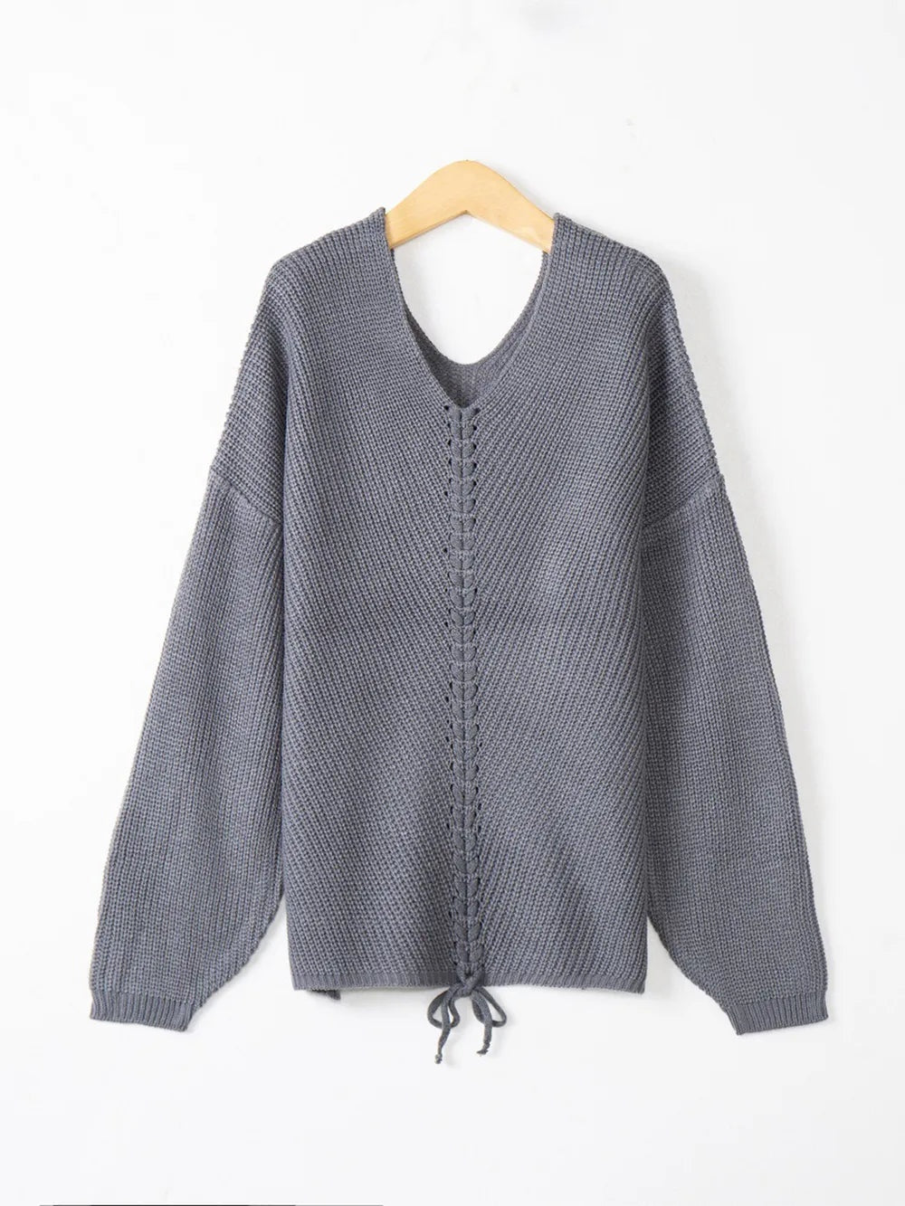 Gray knit lace-up V-neck long sleeve sweater displayed on a hanger, featuring a relaxed silhouette, textured construction, ribbed cuffs, and a tie at the hem.