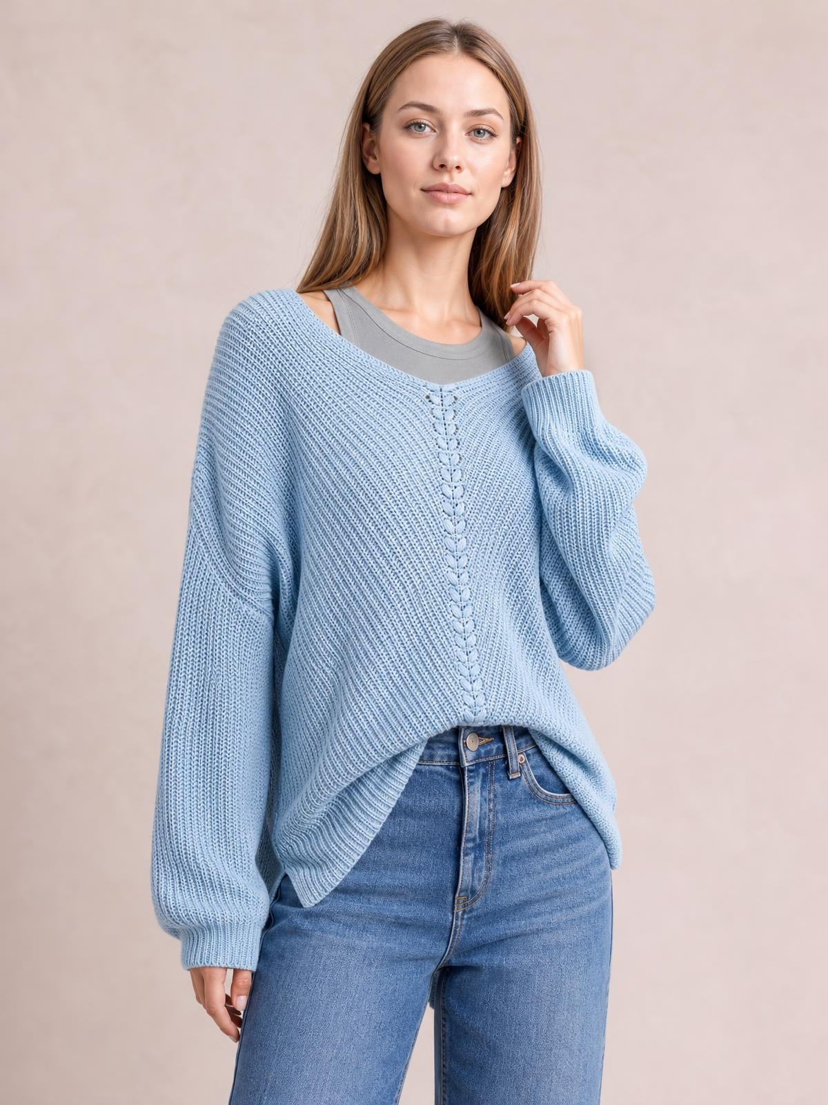 A model wears a light blue lace-up V-neck sweater with long balloon sleeves, ribbed knit texture, relaxed oversized silhouette, and a center cable detail.