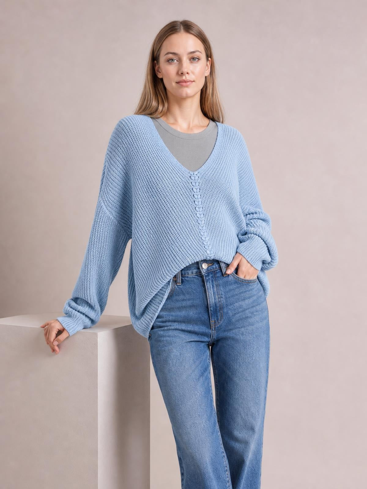 Model wears a light blue lace-up V-neck long sleeve sweater with a relaxed oversized silhouette and textured knit construction, posing with one hand in her jeans pocket.