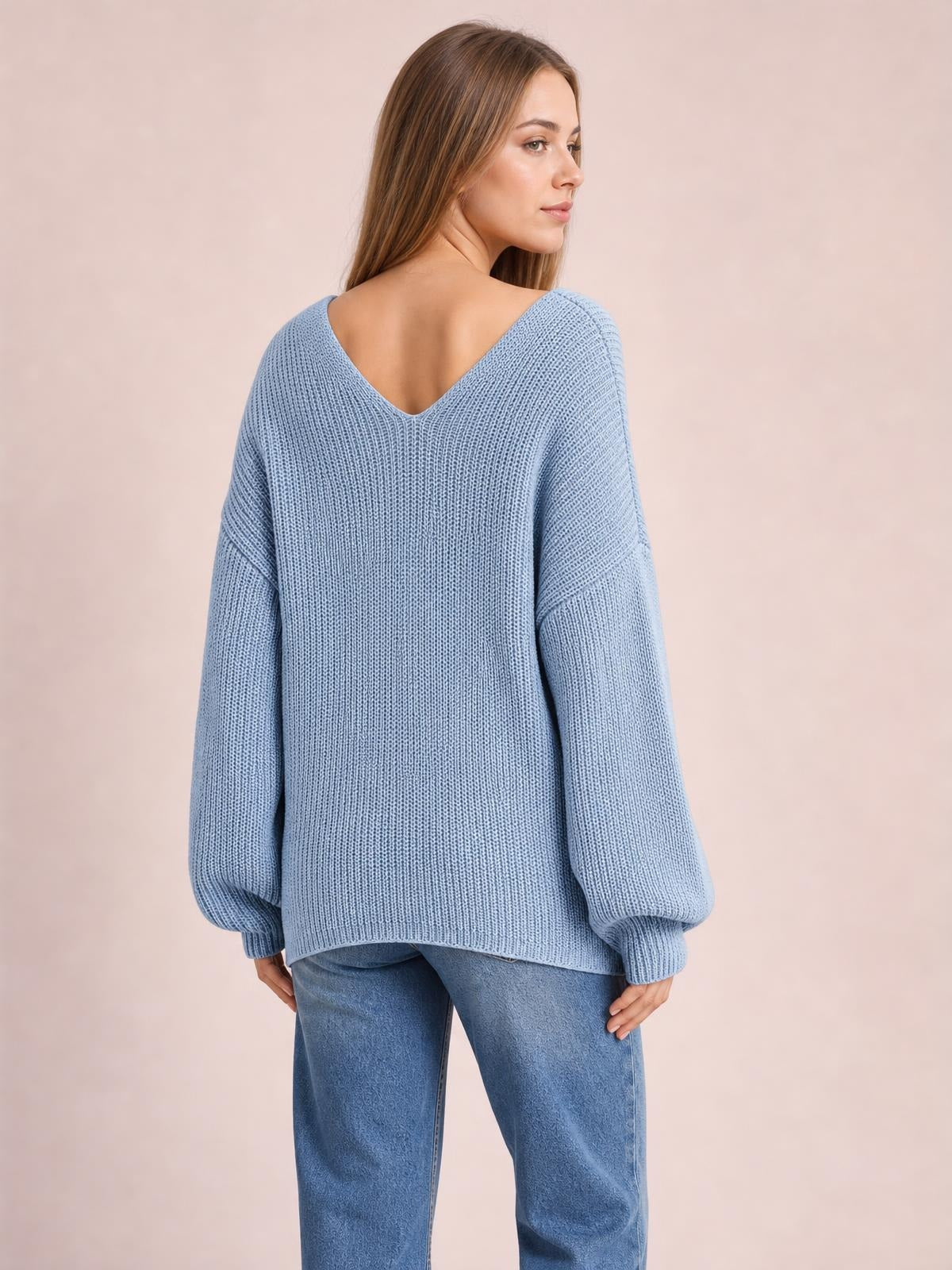 Model looks over her shoulder while wearing a light blue knit sweater with a deep V-neck back, long sleeves, ribbed cuffs, and a relaxed oversized silhouette.