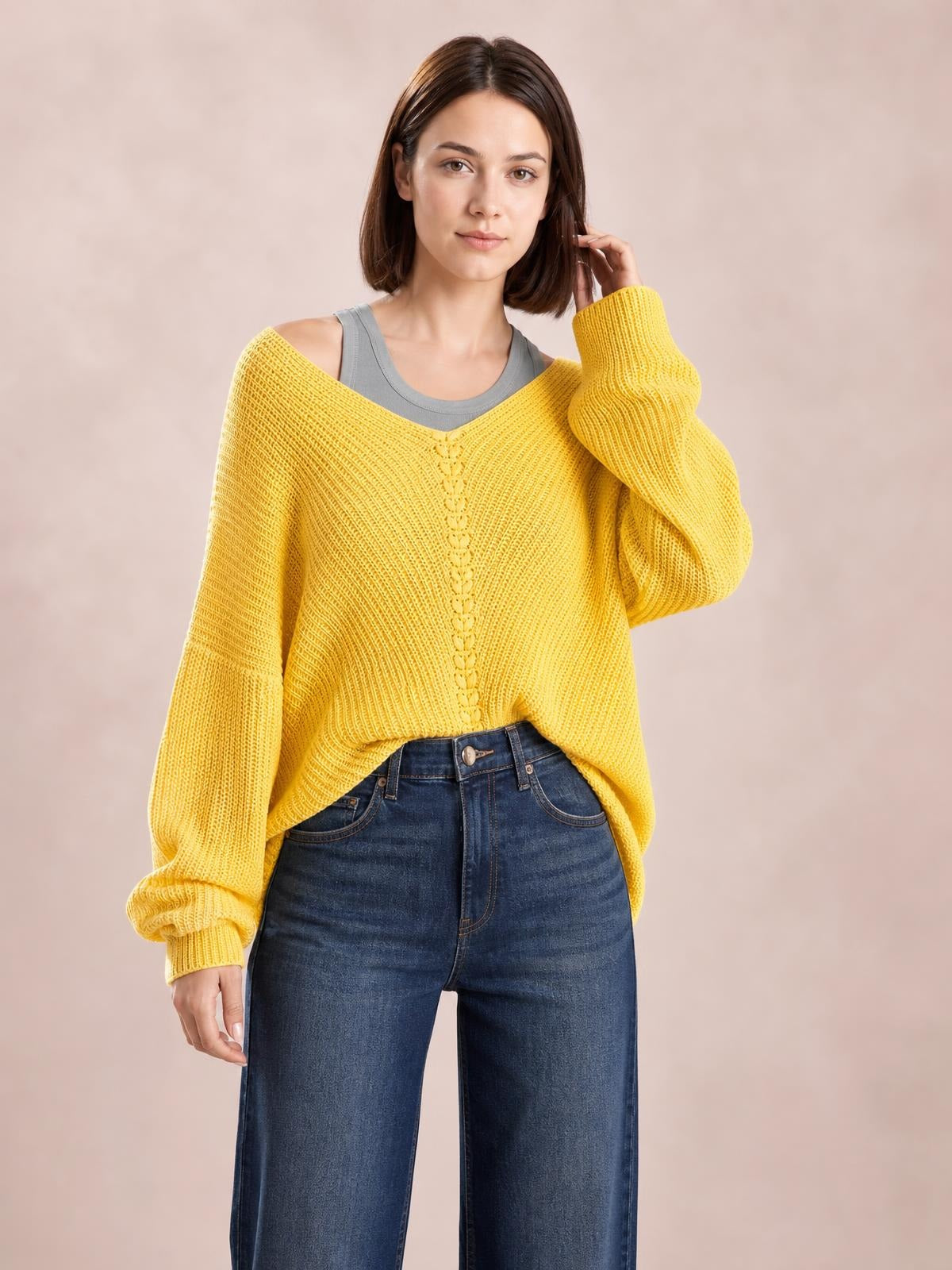 Model wearing a mustard yellow lace-up V-neck long-sleeve sweater with a relaxed silhouette, ribbed knit texture, and one hand raised near her hair.