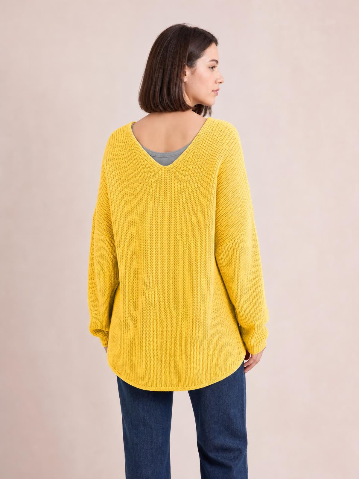 Model shown from the back in a yellow long-sleeve sweater with a ribbed knit texture, relaxed silhouette, deep V-neck, and rounded hem.