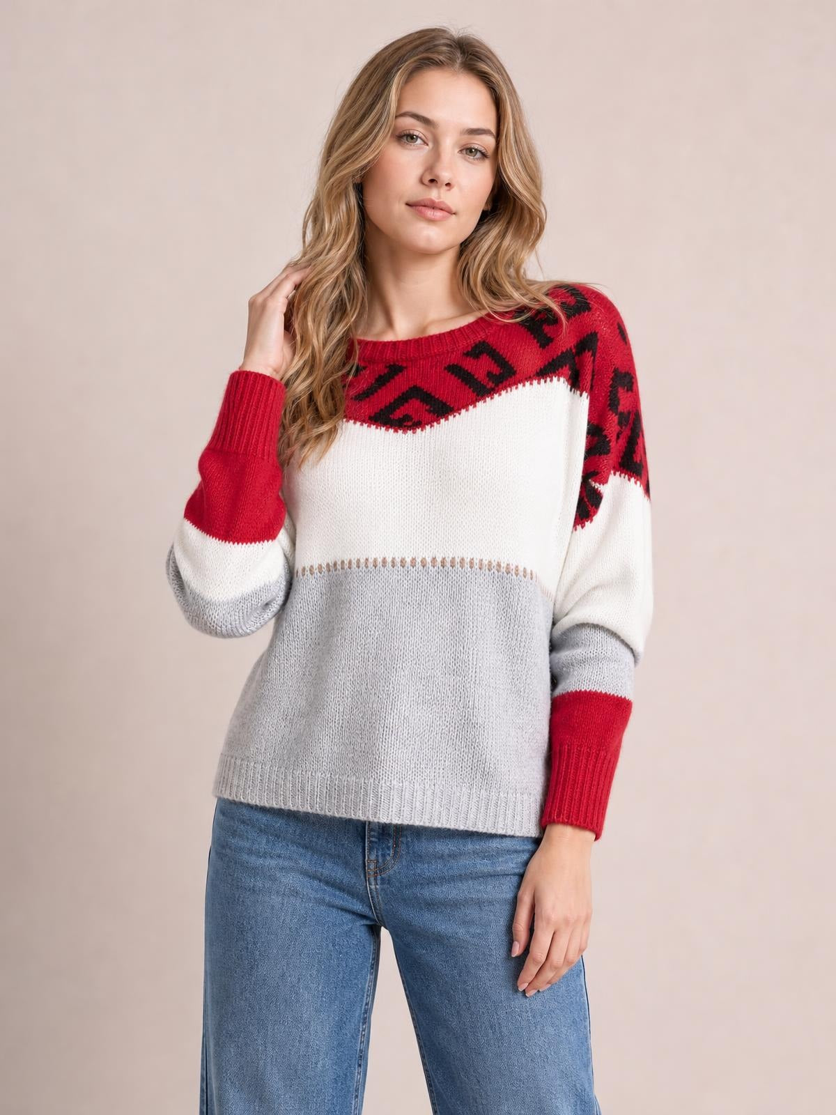Model wearing a relaxed leopard color block long sleeve sweater with red, white, and gray sections, ribbed cuffs and hem, posing with one hand in her hair.