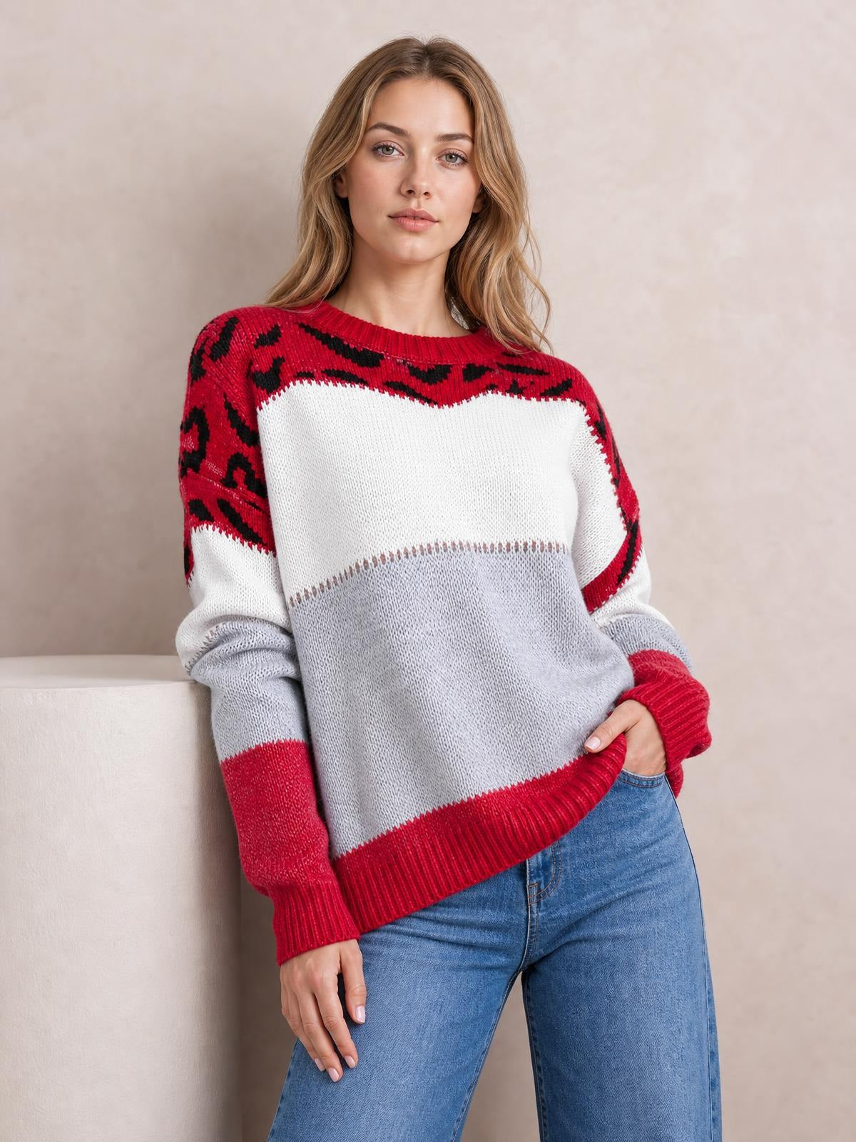 Model leans casually in a relaxed-fit leopard color block sweater with red patterned sleeves, white and gray panels, and ribbed crew neckline, cuffs, and hem.