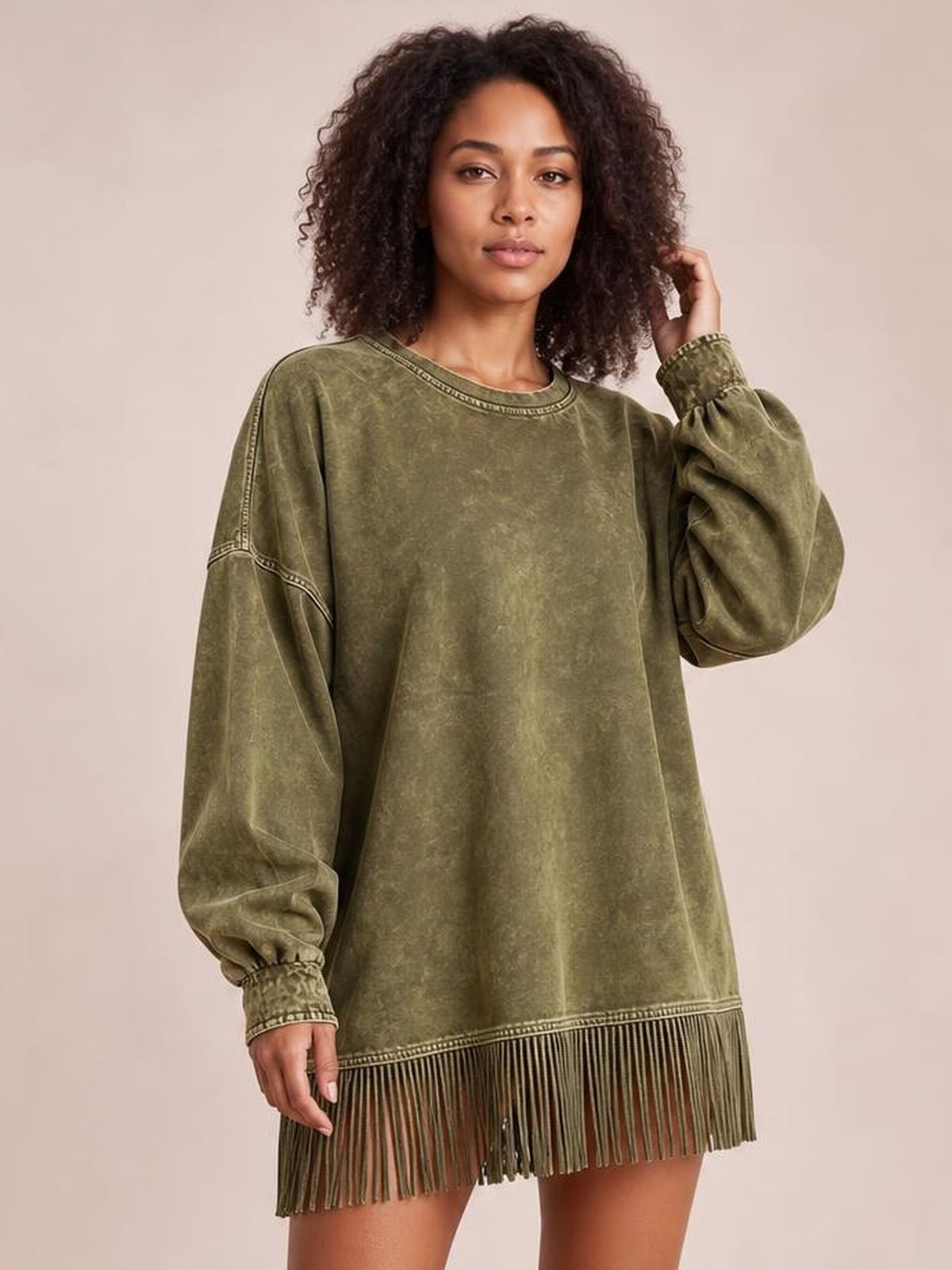 A model poses in an olive green mock-neck mini dress with long sleeves, seam detailing, gathered cuffs, a relaxed silhouette, and a fringed hem.