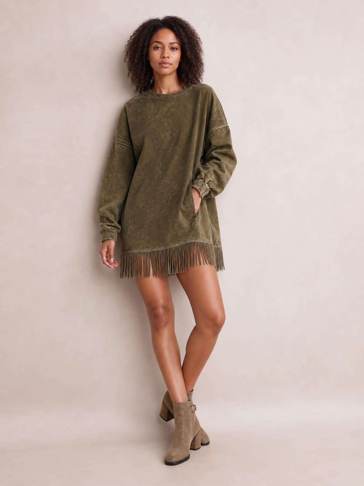 Model wears an olive green long-sleeve mini dress with a relaxed oversized silhouette, crew neckline, seam detailing, side pocket, and fringe hem.
