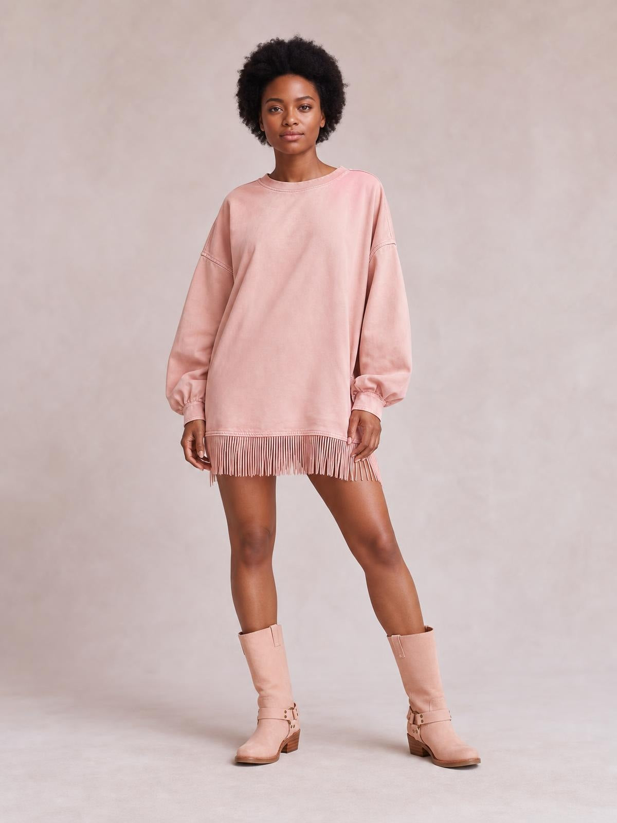 A model stands in a loose pink long-sleeve mini dress with a round neckline, dropped shoulders, gathered cuffs, and a fringe-trimmed hem.