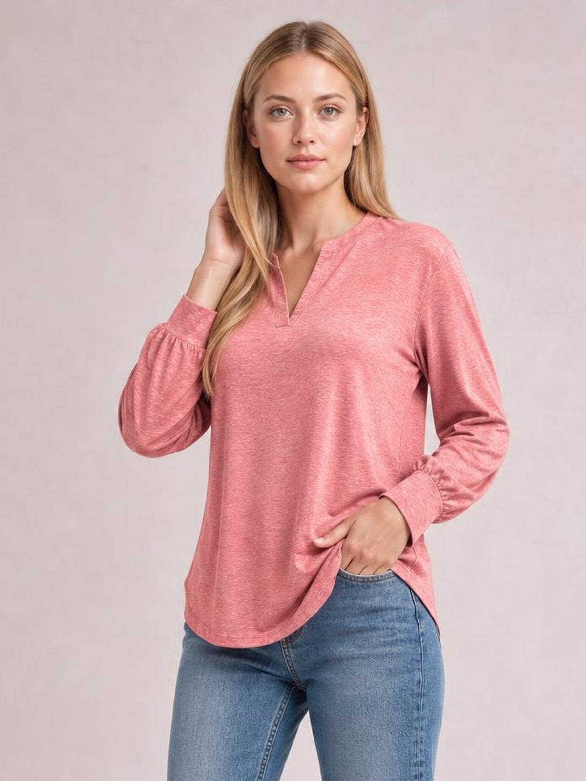Model wearing a pink notched long sleeve T-shirt with a relaxed silhouette, subtle ruffled cuffs, and a curved hem, posing with one hand at her hair.