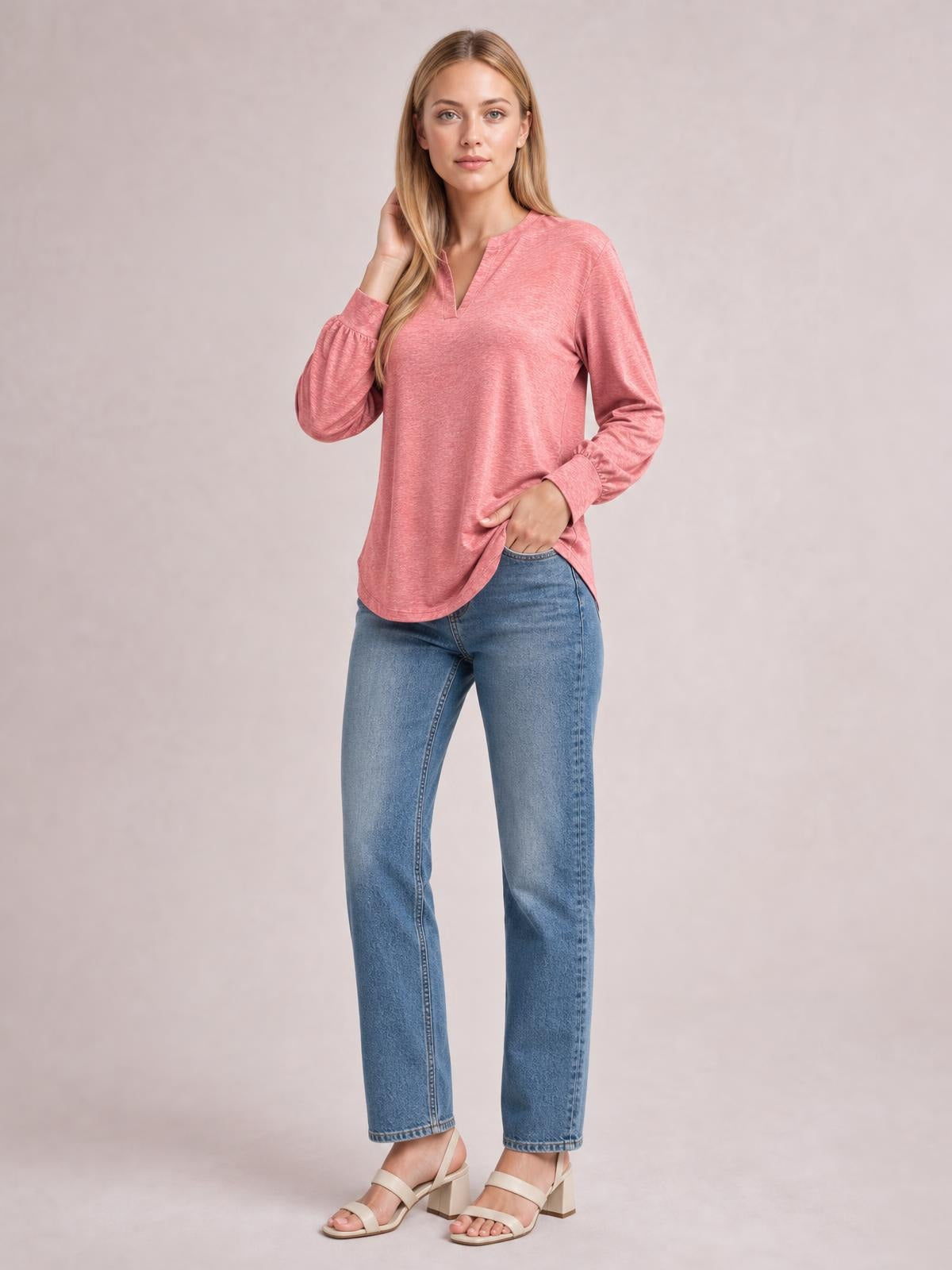 A model poses in a pink notched long sleeve T-shirt with a relaxed silhouette, curved hem, and subtly gathered ruffled cuffs, touching her hair and hem.
