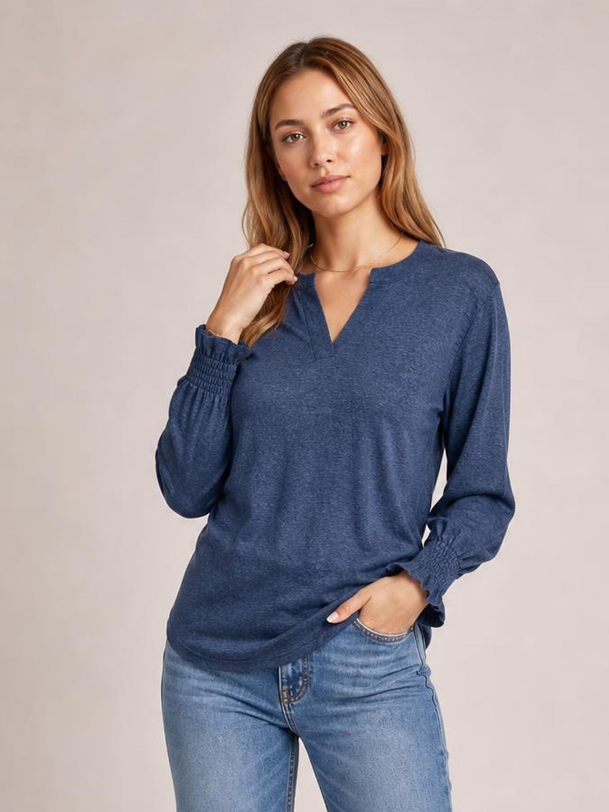 Model poses in a navy notched long sleeve T-shirt with a relaxed silhouette, V-shaped neckline, and gathered ruffled cuffs.
